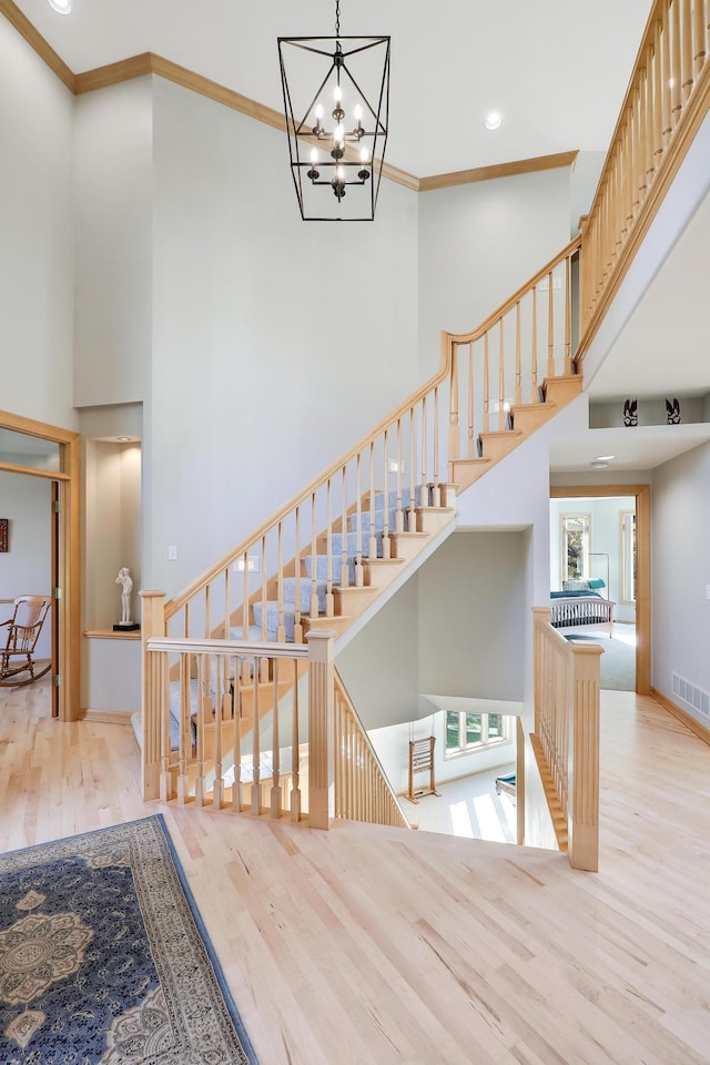 staircase with visible vents, crown molding, a towering ceiling, and wood finished floors