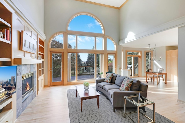 living area with a tiled fireplace, a high ceiling, crown molding, light wood-style floors, and a notable chandelier