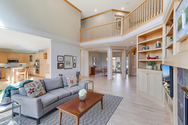 living room with a towering ceiling, light wood-style flooring, ornamental molding, and recessed lighting