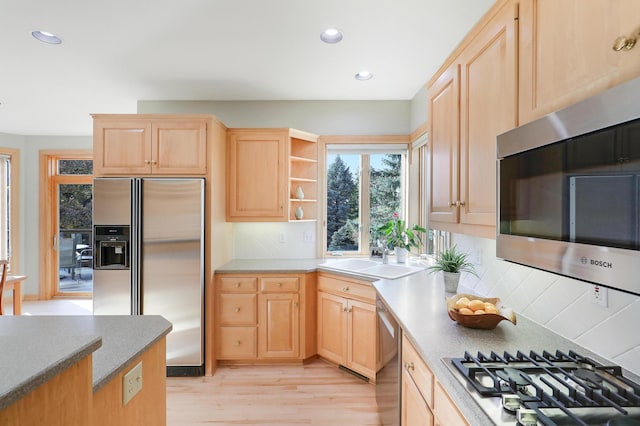 kitchen with backsplash, appliances with stainless steel finishes, light wood-style floors, light brown cabinets, and a sink