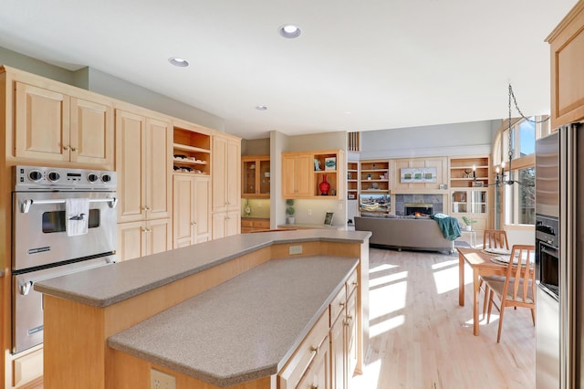 kitchen featuring a center island, open shelves, stainless steel appliances, light brown cabinets, and a warm lit fireplace