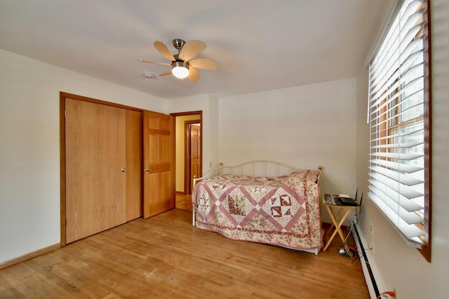 bedroom with ceiling fan, a closet, wood-type flooring, and a baseboard heating unit