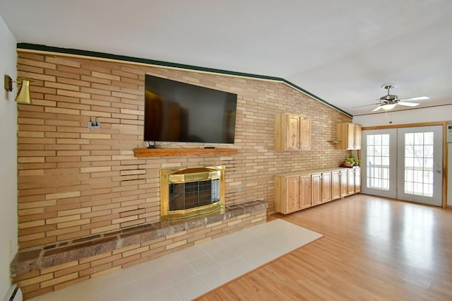 unfurnished living room with a brick fireplace, light hardwood / wood-style flooring, ceiling fan, vaulted ceiling, and brick wall