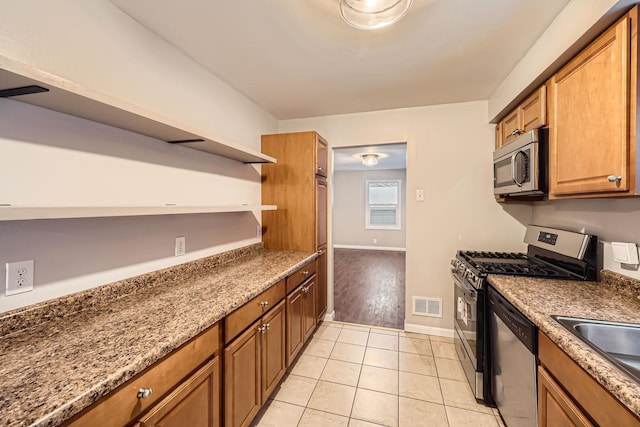 kitchen with appliances with stainless steel finishes, sink, stone countertops, and light tile patterned flooring