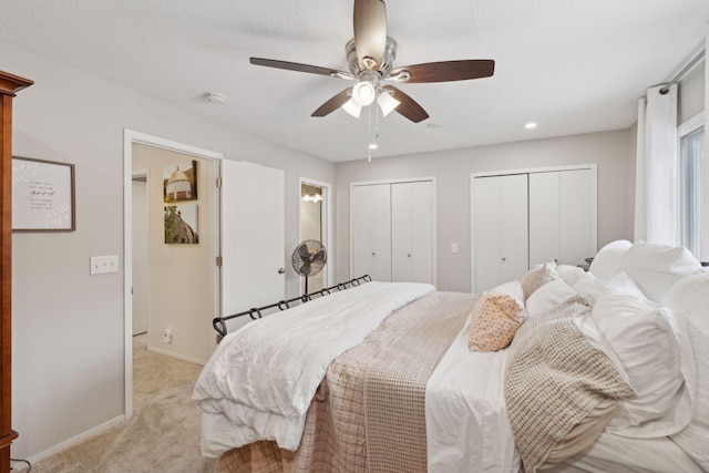 bedroom with ceiling fan, light colored carpet, and multiple closets