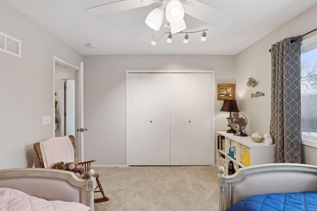 bedroom featuring ceiling fan, light colored carpet, a textured ceiling, and a closet