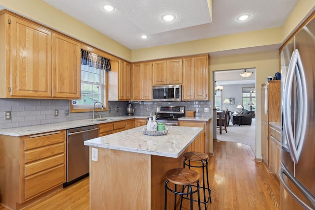 kitchen with sink, light stone counters, a center island, appliances with stainless steel finishes, and decorative backsplash