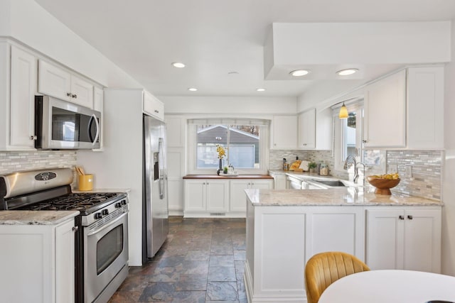 kitchen with white cabinetry, light stone countertops, sink, stainless steel appliances, and kitchen peninsula