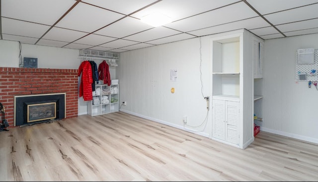 basement with a paneled ceiling, built in shelves, light wood-type flooring, and a brick fireplace