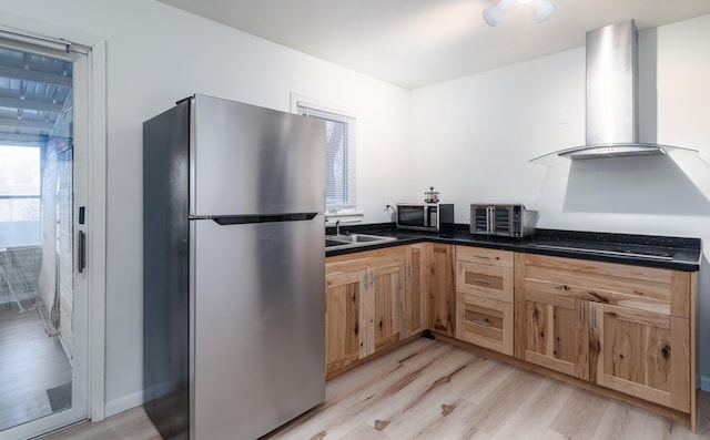 kitchen with wall chimney range hood, sink, light hardwood / wood-style flooring, black stovetop, and stainless steel fridge