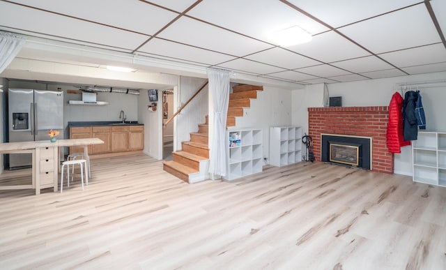 basement featuring sink, a drop ceiling, light hardwood / wood-style flooring, stainless steel refrigerator with ice dispenser, and a fireplace