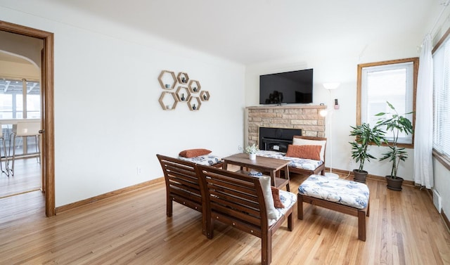 living room featuring a stone fireplace, light wood-style flooring, and baseboards