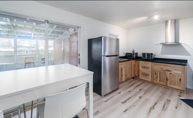 kitchen featuring wall chimney range hood, stainless steel refrigerator, and light hardwood / wood-style flooring