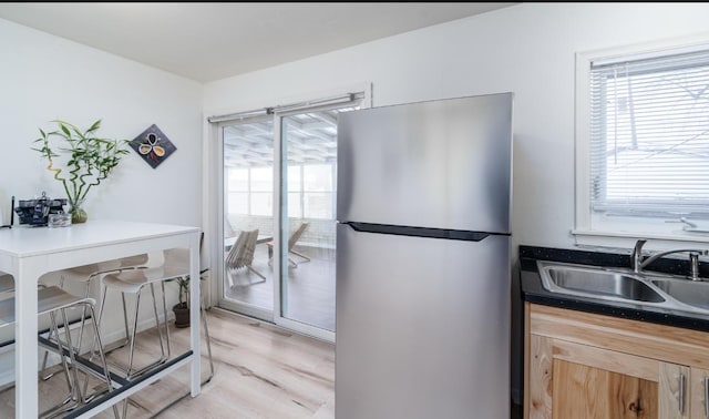 kitchen featuring light brown cabinets, light wood-type flooring, stainless steel refrigerator, and sink