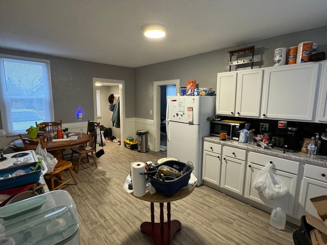 kitchen featuring light stone countertops, white refrigerator, light wood-type flooring, and white cabinetry