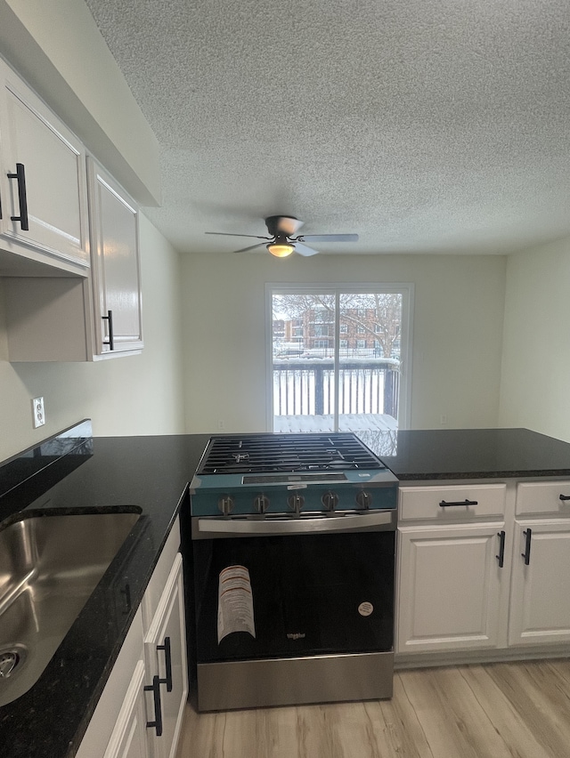 kitchen featuring white cabinets, ceiling fan, sink, and stainless steel stove