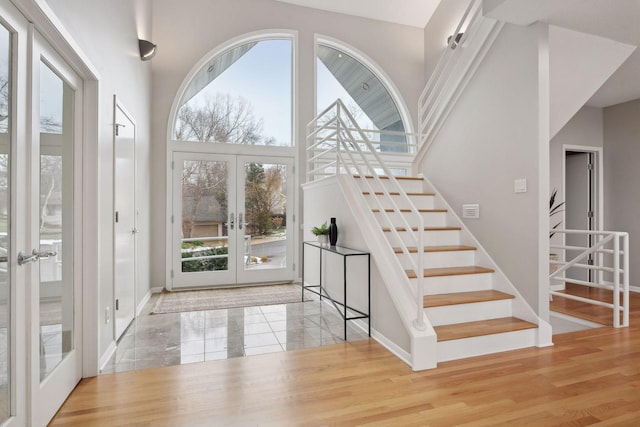 entrance foyer with french doors, a towering ceiling, and wood-type flooring