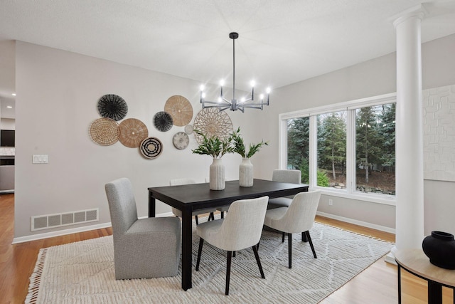 dining area with decorative columns, a chandelier, and light wood-type flooring