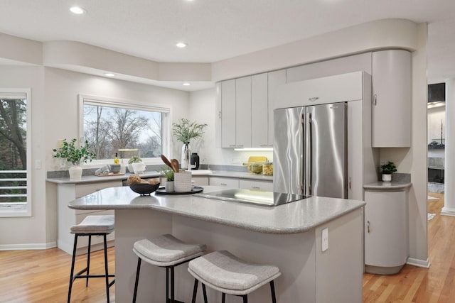 kitchen with light hardwood / wood-style flooring, a breakfast bar area, stainless steel refrigerator, a center island, and white cabinets