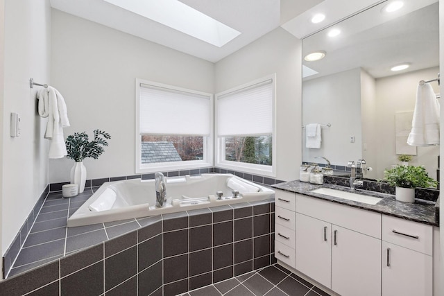 bathroom featuring tile patterned flooring, tiled tub, vanity, and a skylight