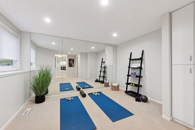 exercise area featuring light carpet and a textured ceiling