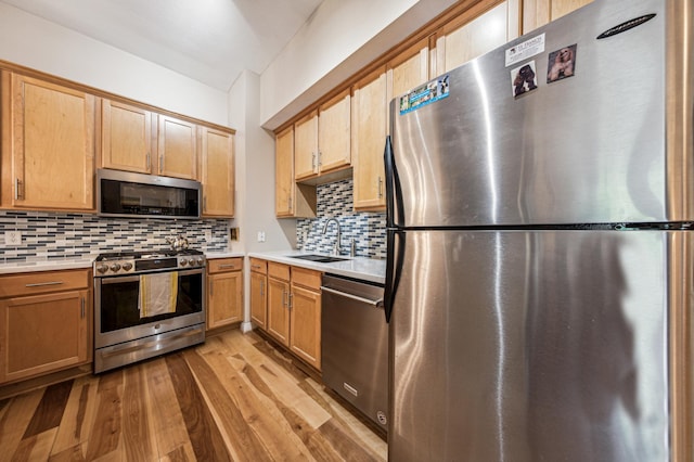 kitchen with tasteful backsplash, appliances with stainless steel finishes, sink, and light hardwood / wood-style floors