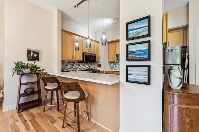 kitchen with pendant lighting, a breakfast bar, decorative backsplash, kitchen peninsula, and light wood-type flooring