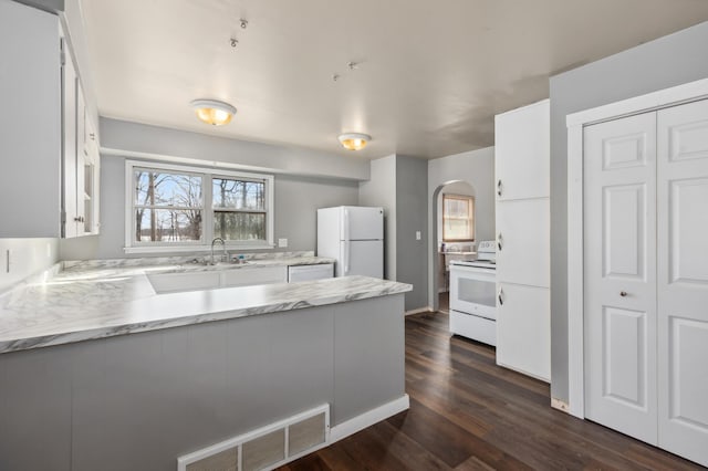 kitchen with visible vents, white appliances, arched walkways, a peninsula, and white cabinets