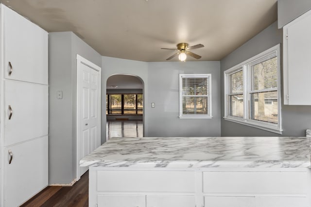 kitchen with arched walkways, dark wood-style floors, white cabinets, and ceiling fan