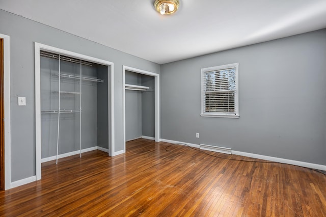 unfurnished bedroom featuring hardwood / wood-style floors, visible vents, baseboards, and multiple closets