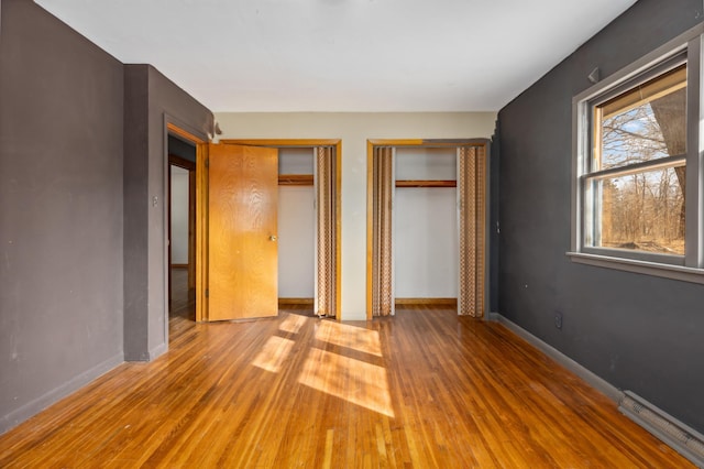 unfurnished bedroom featuring wood finished floors, multiple closets, and baseboards