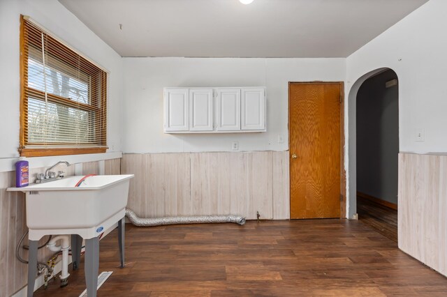 unfurnished room with arched walkways, dark wood-style flooring, and wainscoting