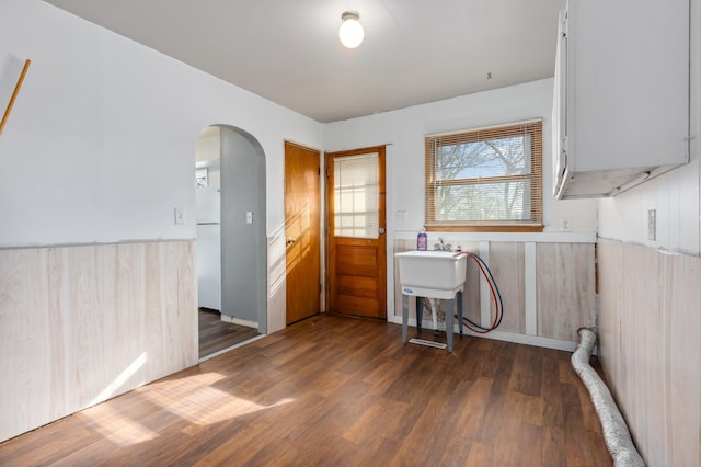 clothes washing area with wooden walls, a wainscoted wall, laundry area, wood finished floors, and arched walkways