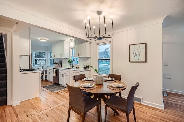 dining room featuring light wood-type flooring, a notable chandelier, a healthy amount of sunlight, and sink