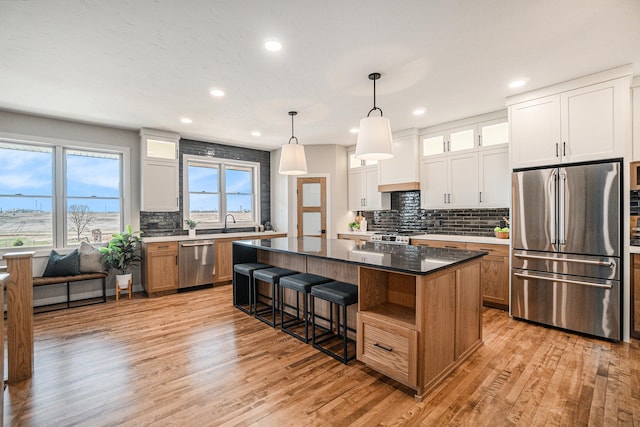 kitchen with pendant lighting, white cabinets, light hardwood / wood-style flooring, a kitchen island, and stainless steel appliances