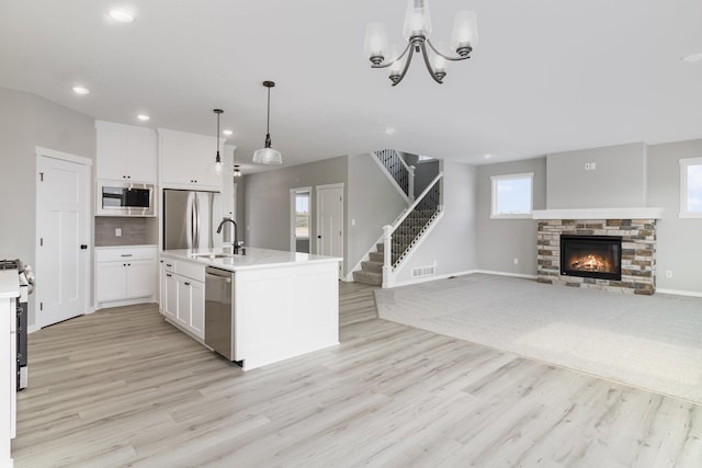 kitchen featuring appliances with stainless steel finishes, white cabinets, a kitchen island with sink, a fireplace, and hanging light fixtures