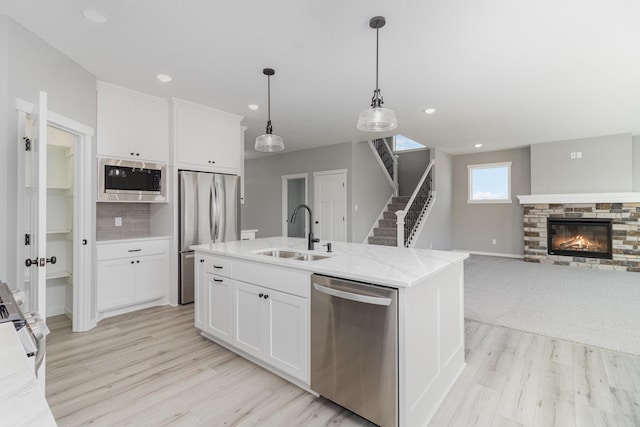 kitchen with stainless steel appliances, sink, a center island with sink, white cabinetry, and hanging light fixtures