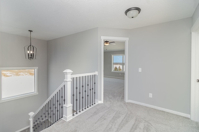 hallway with light colored carpet, a textured ceiling, and a notable chandelier