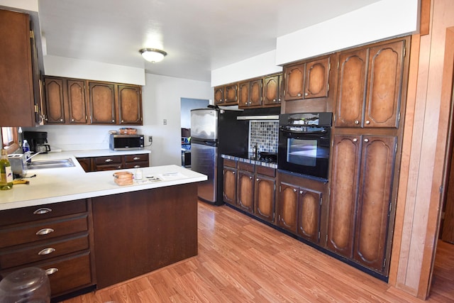 kitchen with dark brown cabinetry, light wood-type flooring, tasteful backsplash, kitchen peninsula, and stainless steel appliances