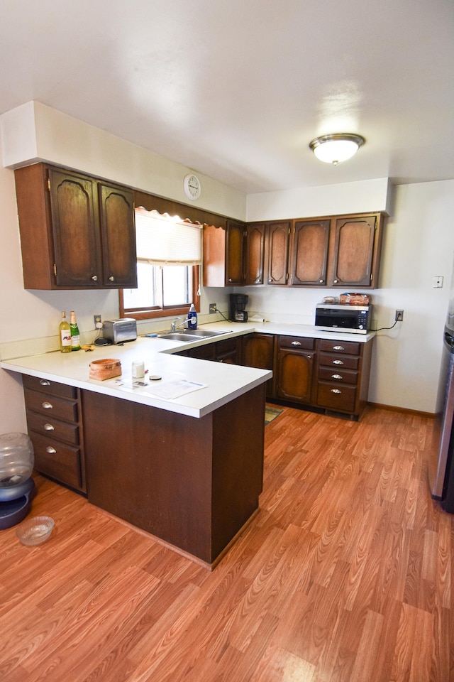 kitchen featuring light hardwood / wood-style floors, dark brown cabinetry, kitchen peninsula, and sink