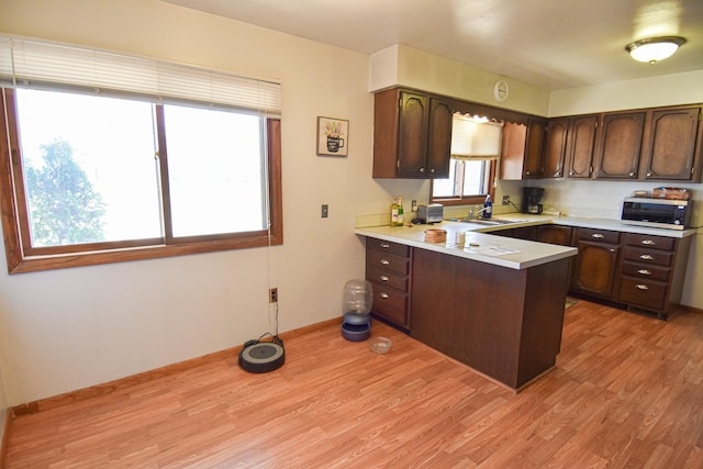 kitchen with kitchen peninsula, sink, dark brown cabinets, and light wood-type flooring