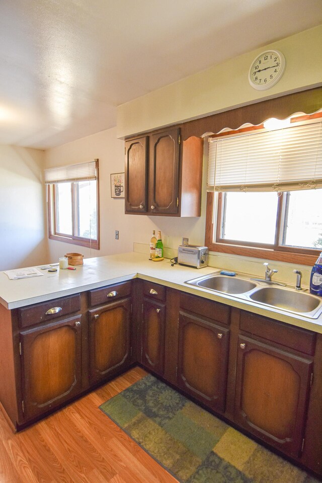 kitchen featuring dark brown cabinets, light hardwood / wood-style floors, kitchen peninsula, and sink