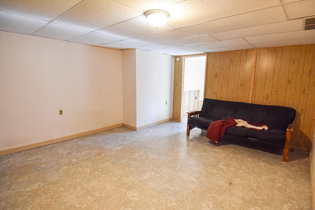 living area featuring a drop ceiling and wooden walls