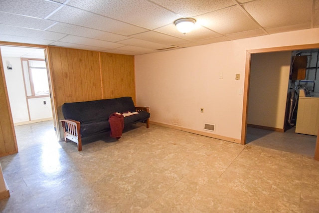 living area featuring a paneled ceiling and wood walls