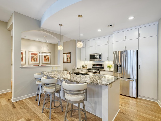 kitchen with light wood finished floors, appliances with stainless steel finishes, white cabinetry, a sink, and a kitchen breakfast bar