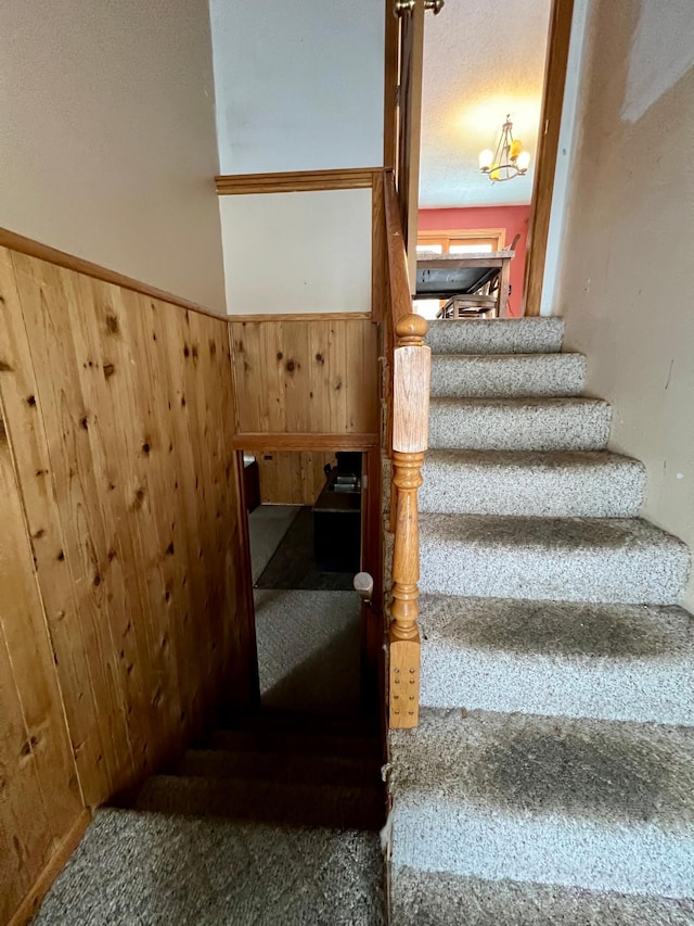 stairway featuring a chandelier, a textured ceiling, carpet floors, and wood walls