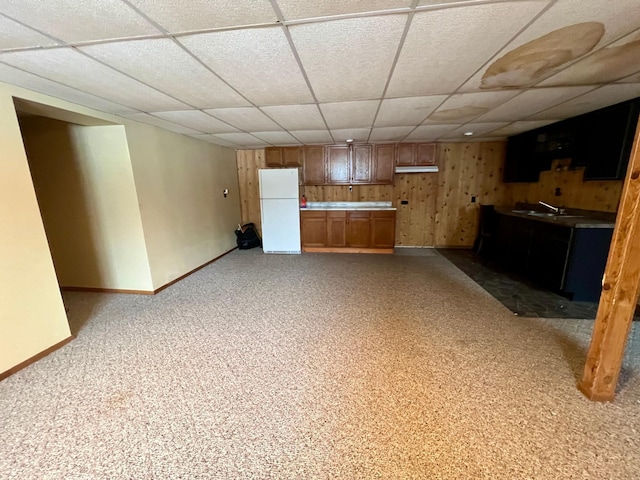 basement featuring carpet, a drop ceiling, wooden walls, sink, and white refrigerator