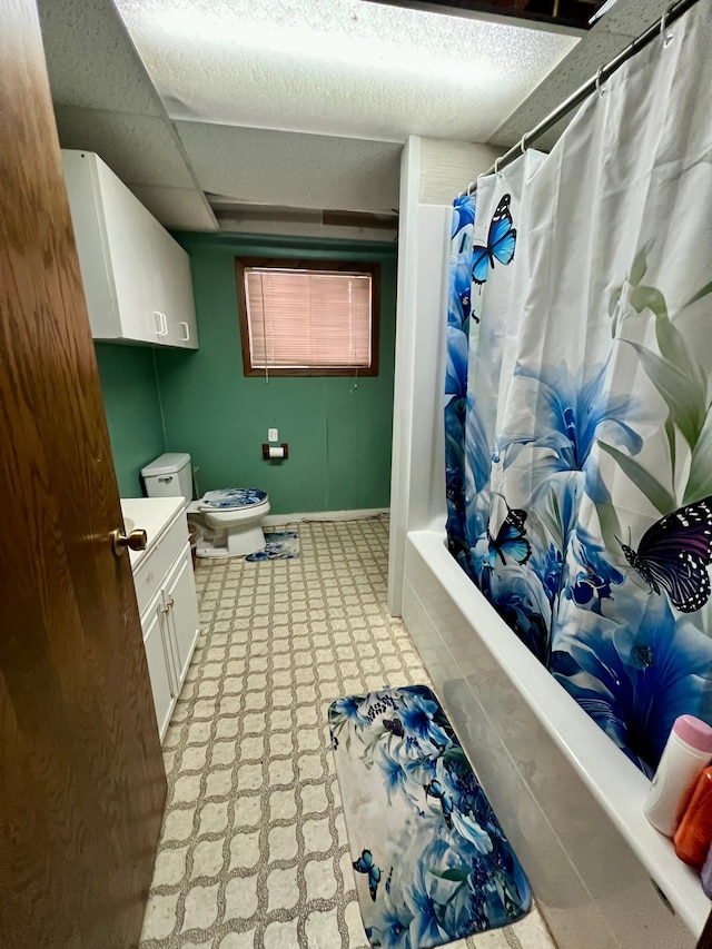 full bathroom with shower / bath combo with shower curtain, a drop ceiling, vanity, and toilet