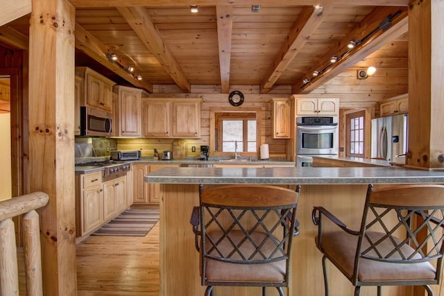 kitchen with appliances with stainless steel finishes, light brown cabinetry, track lighting, and a kitchen breakfast bar