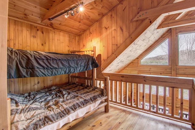 bedroom featuring wood walls, lofted ceiling with beams, light hardwood / wood-style floors, and track lighting